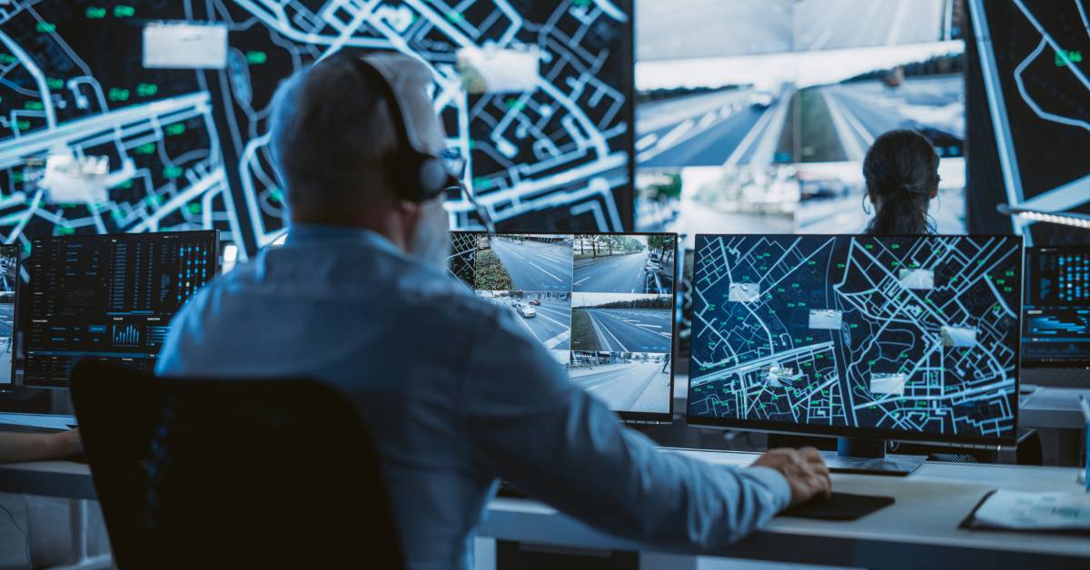 A fleet management specialist in a room surrounded by computers uses headphones and a microphone to monitor deliveries.